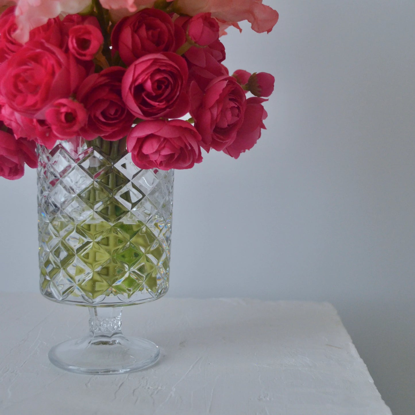 Clear glass vase with pink flowers on a white surface