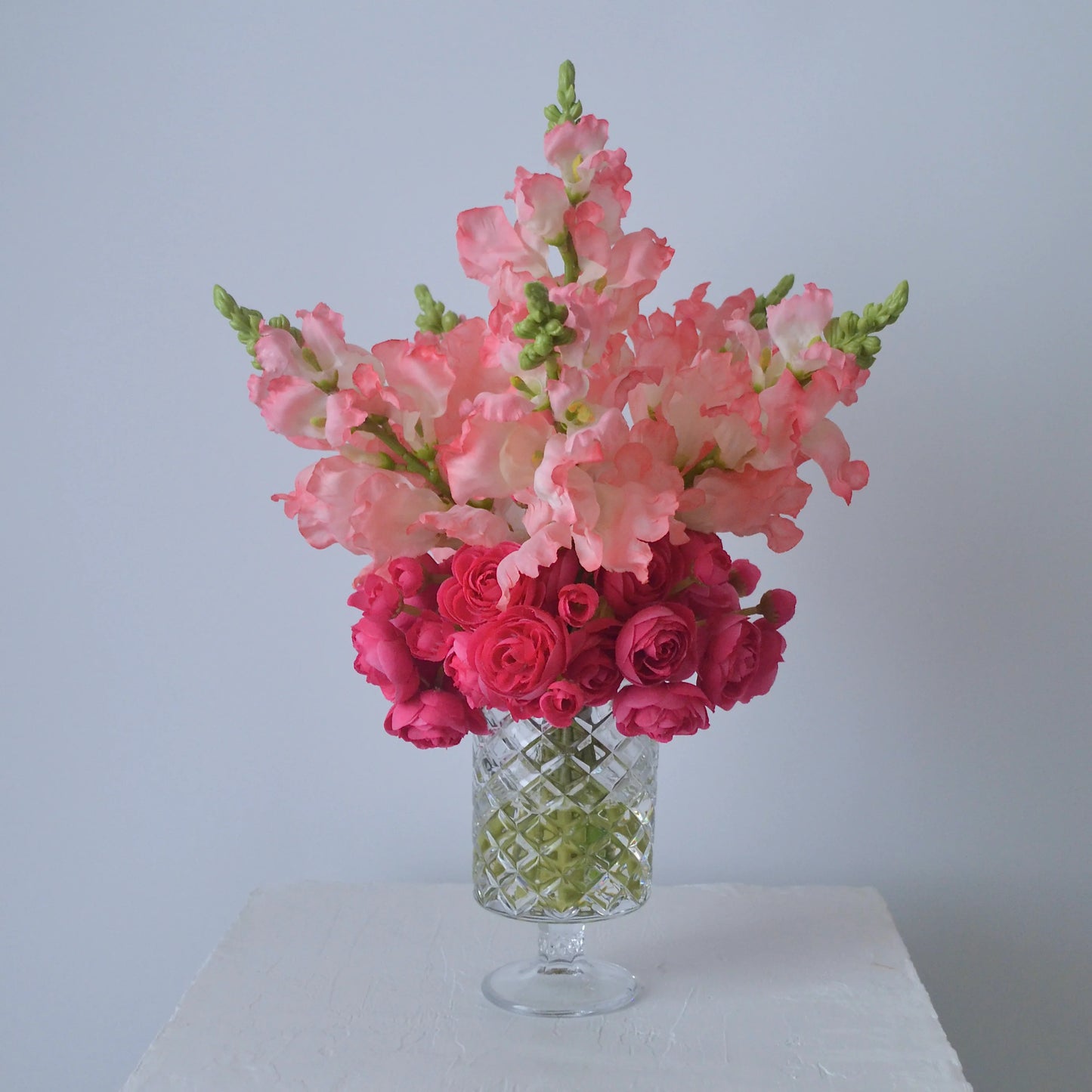 Bouquet of pink and red flowers in a clear glass vase on a white surface with a light gray background