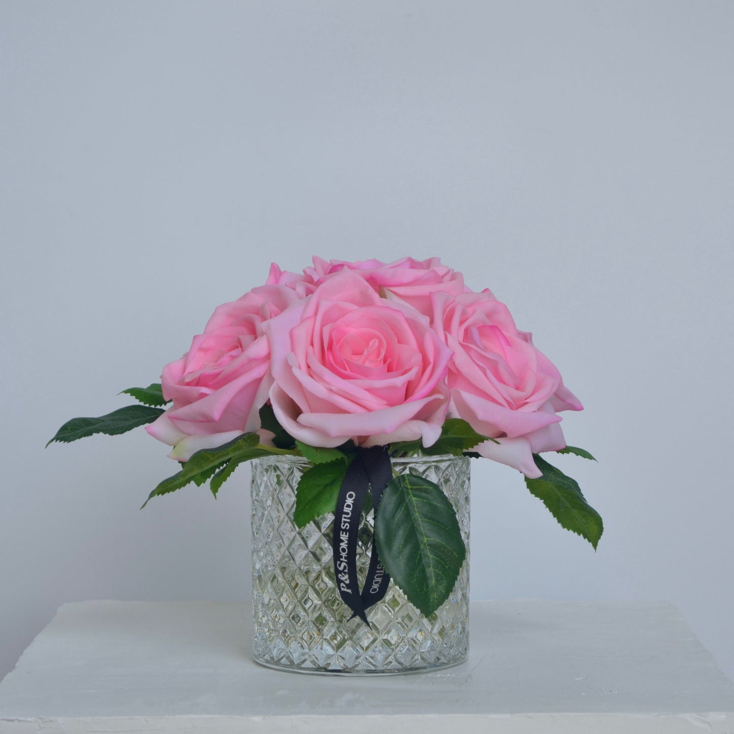Glass vase with pink roses on a white surface against a light gray background