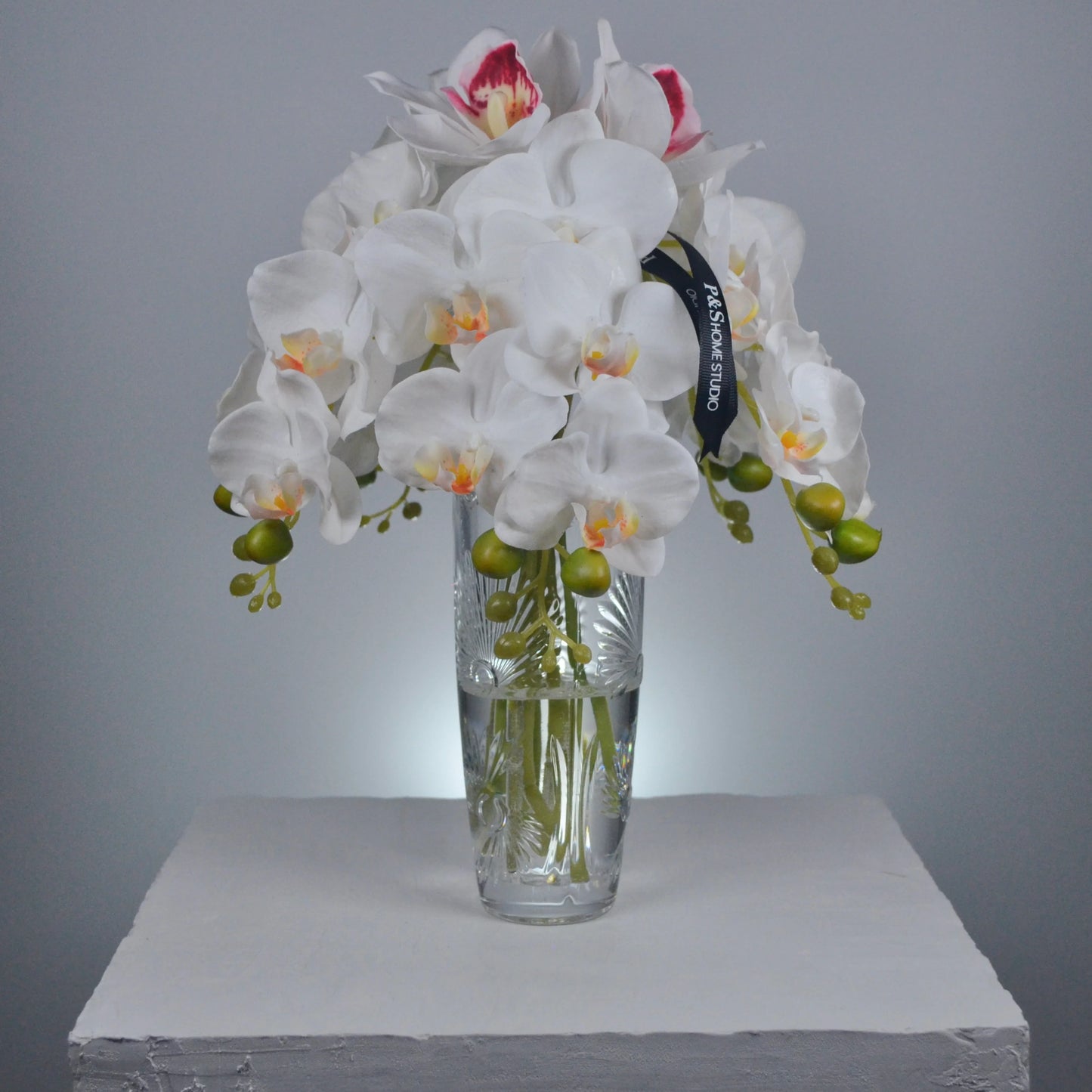 Bouquet of white orchids with green stems in a clear glass vase on a gray background