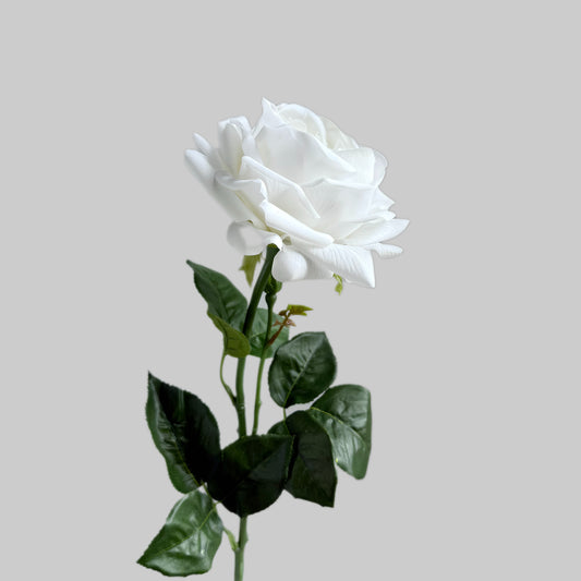 White artificial rose with green leaves on a light gray background