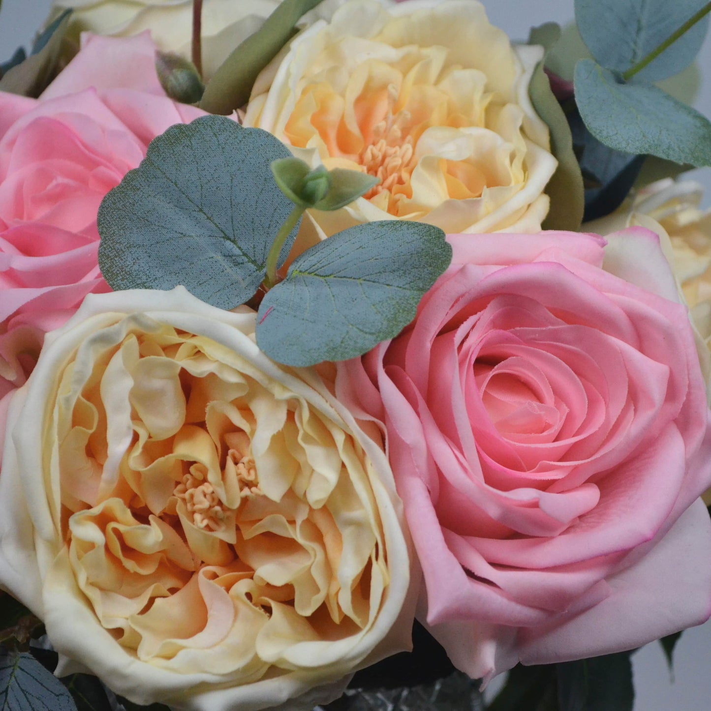 Bouquet of pink, yellow, and white roses with green leaves.
