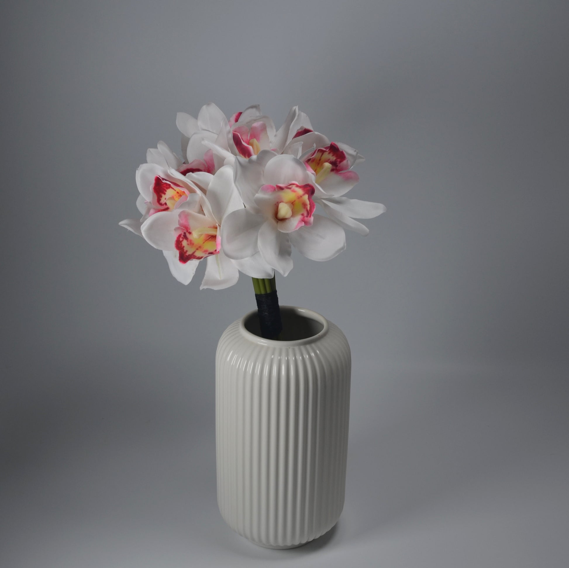 White ribbed vase with artificial flowers on a gray background
