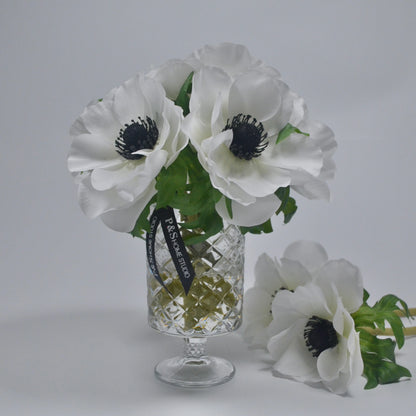 White flowers with green leaves in a clear glass vase on a light gray background