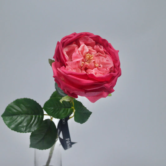 Pink artificial rose with green leaves on a gray background