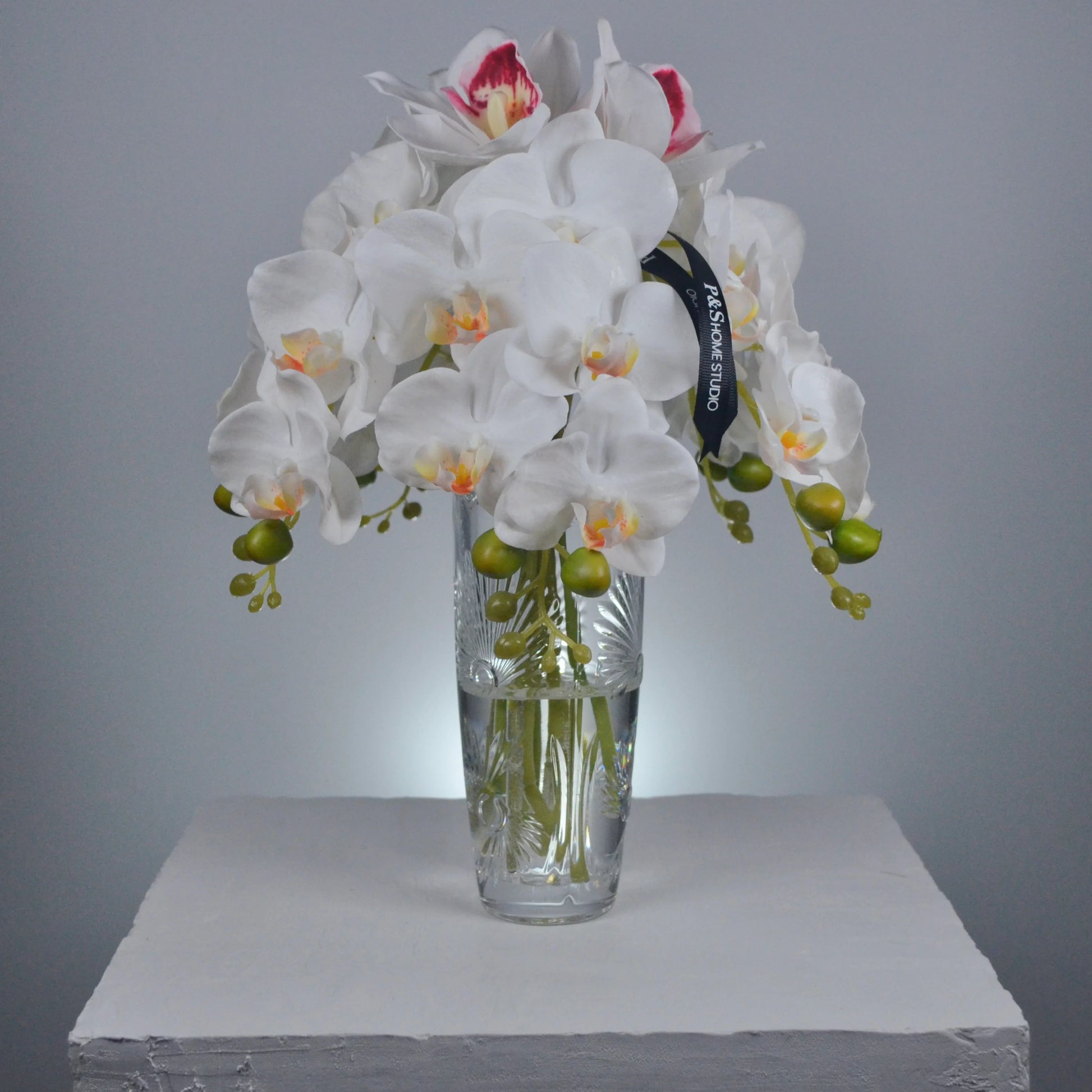 Bouquet of white orchids with green stems in a clear glass vase on a gray background